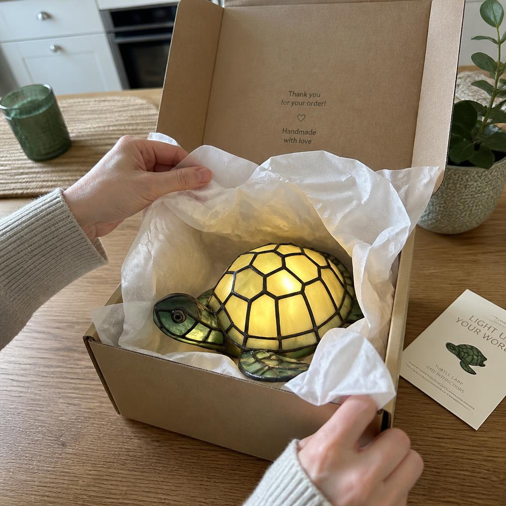 Hände packen die LeuchtSchildkröte aus einem Karton mit Seidenpapier aus